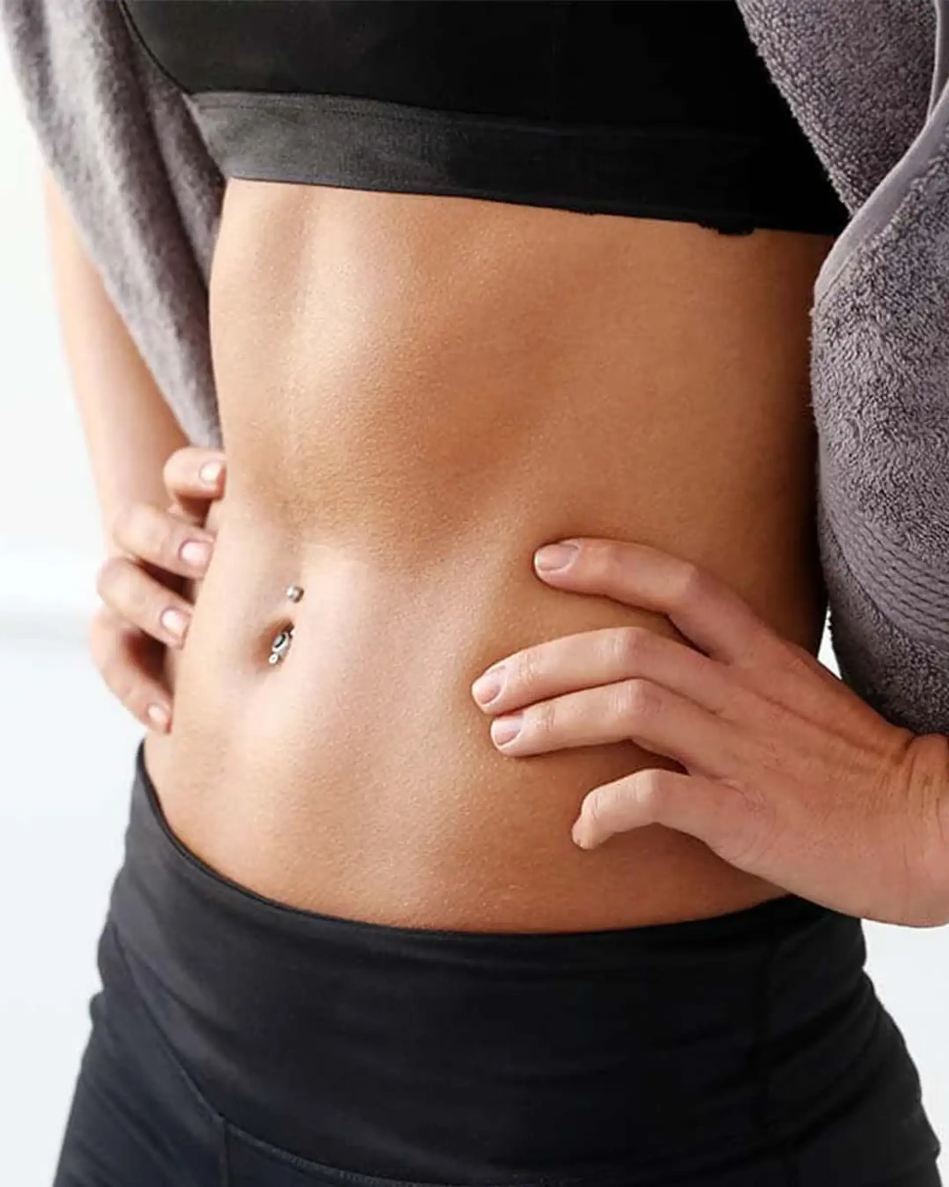 Donna con pancia piatta e piercing all'ombelico in abbigliamento sportivo.